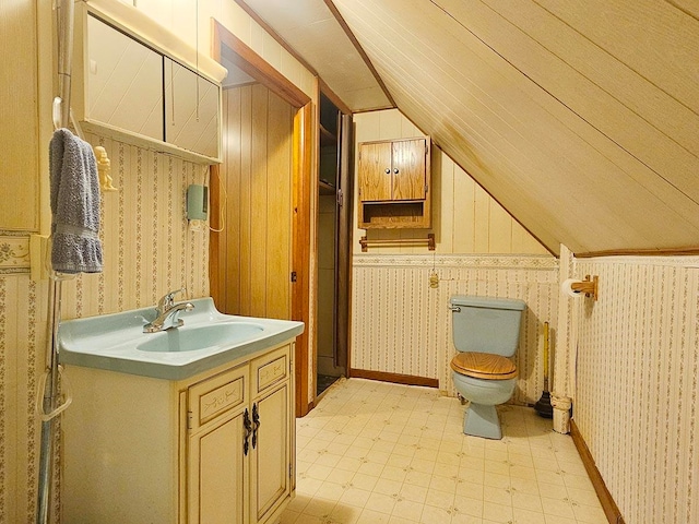 bathroom featuring wood walls, vaulted ceiling, toilet, and vanity