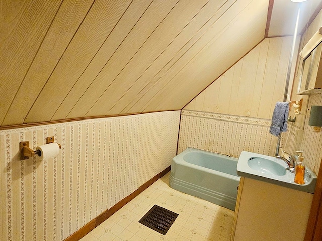 bathroom featuring a bathtub, wooden walls, lofted ceiling, and vanity