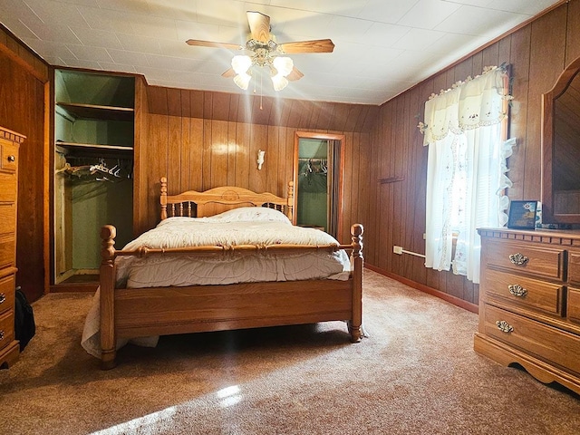 carpeted bedroom with ceiling fan, wooden walls, a closet, and a spacious closet