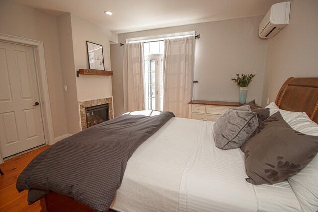 bedroom featuring a wall mounted air conditioner, a tile fireplace, and hardwood / wood-style floors