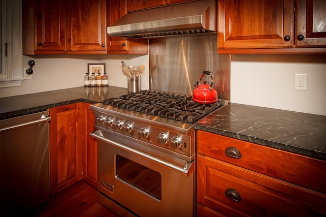 kitchen featuring stainless steel dishwasher, dark stone counters, dark wood-type flooring, gas range oven, and wall chimney exhaust hood