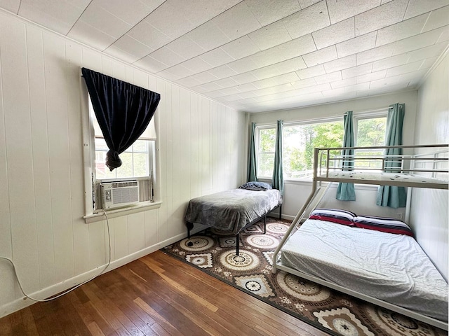 bedroom featuring wood-type flooring, cooling unit, and wooden walls