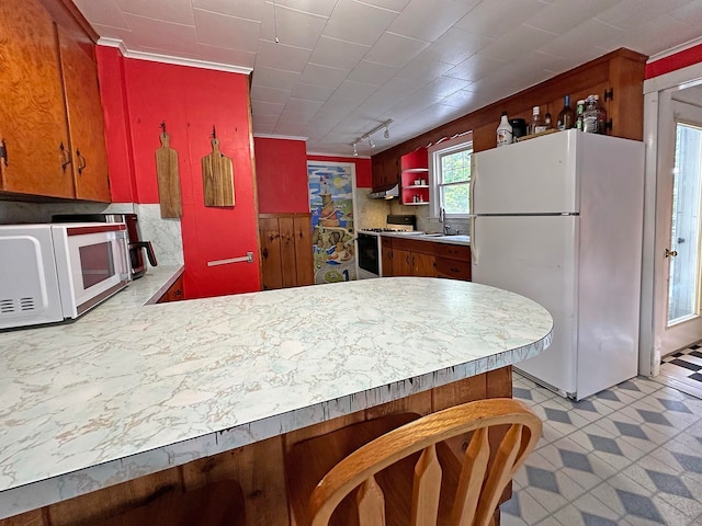 kitchen with white appliances, sink, range hood, and kitchen peninsula