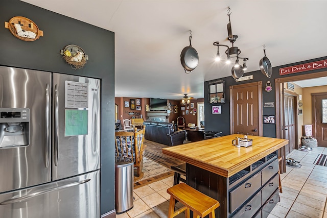 kitchen featuring wood counters, stainless steel fridge, a center island, light tile patterned floors, and ceiling fan