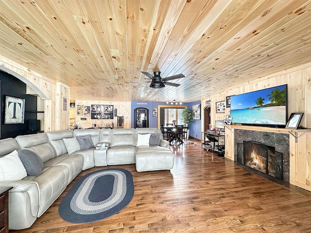 living area with a ceiling fan, wooden ceiling, wood finished floors, a lit fireplace, and wood walls