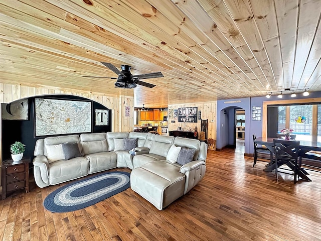 living area featuring wooden walls, arched walkways, wood ceiling, wood finished floors, and track lighting