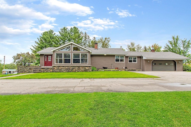 view of front facade featuring a chimney, an attached garage, stone siding, driveway, and a front lawn