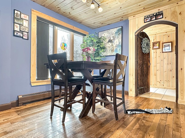 dining space with wooden walls, baseboards, arched walkways, wood ceiling, and wood finished floors