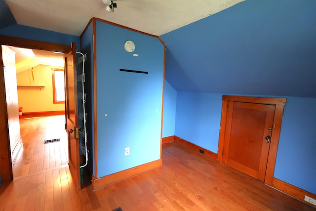 additional living space featuring vaulted ceiling, light hardwood / wood-style flooring, and a textured ceiling