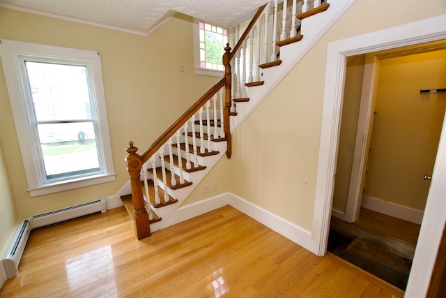 stairway featuring hardwood / wood-style flooring, crown molding, and a baseboard heating unit