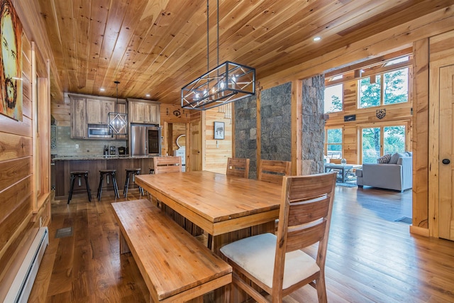 dining room featuring wood walls, dark wood-type flooring, a baseboard heating unit, and a towering ceiling