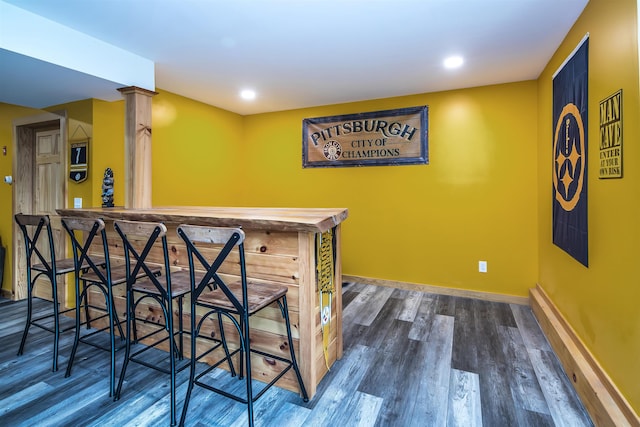 bar featuring dark wood-type flooring and decorative columns