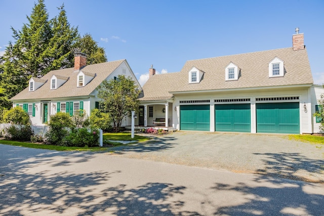 cape cod home featuring a chimney, an attached garage, roof with shingles, and gravel driveway