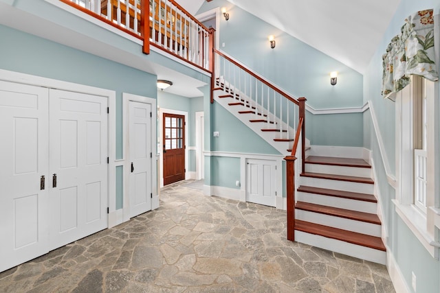 entryway featuring a decorative wall, a towering ceiling, stone flooring, a wainscoted wall, and stairs
