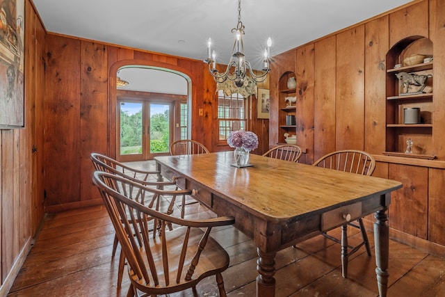 dining space with a chandelier, wood walls, arched walkways, built in shelves, and hardwood / wood-style flooring