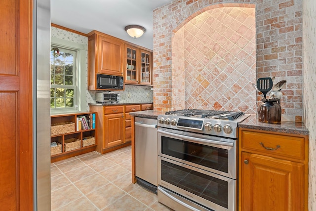 kitchen with light tile patterned floors, glass insert cabinets, brown cabinets, stainless steel appliances, and decorative backsplash