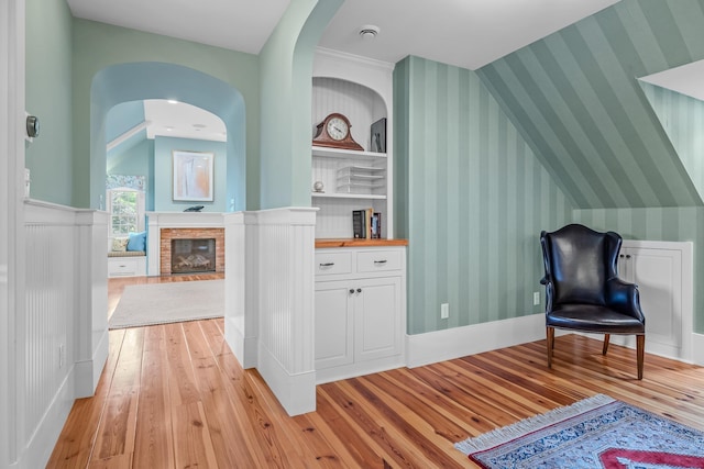 sitting room featuring a fireplace, arched walkways, light wood-style floors, and wallpapered walls