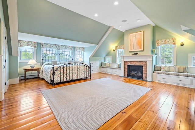 bedroom with a fireplace with flush hearth, vaulted ceiling, recessed lighting, baseboard heating, and light wood finished floors