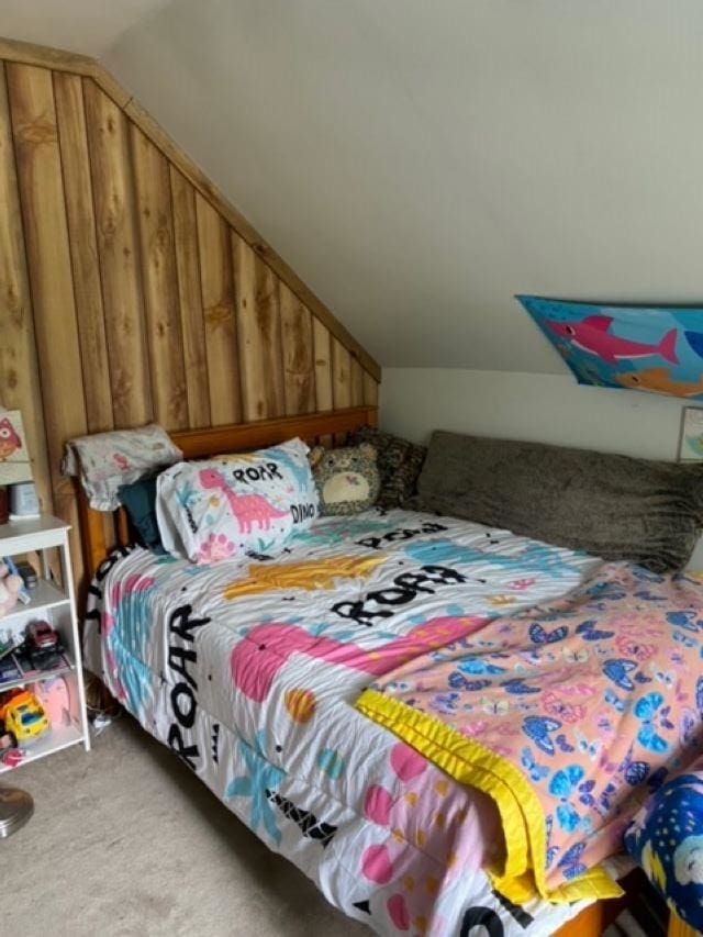 carpeted bedroom featuring wood walls and vaulted ceiling