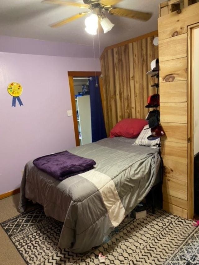 carpeted bedroom with ceiling fan and wooden walls