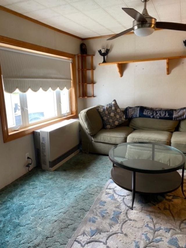 carpeted living room with ceiling fan, heating unit, and ornamental molding