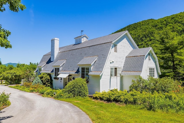 view of home's exterior featuring a gambrel roof, a forest view, and a chimney