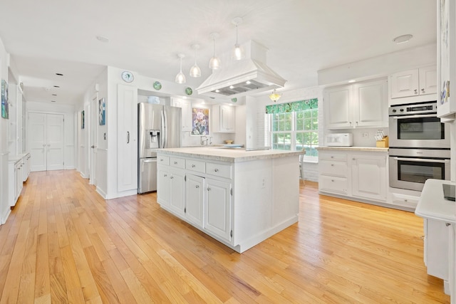 kitchen featuring island range hood, light wood-style flooring, light countertops, white cabinets, and appliances with stainless steel finishes