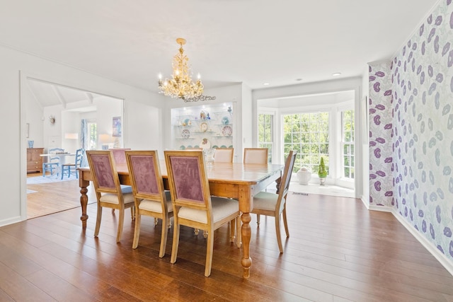 dining space with dark wood finished floors, wallpapered walls, an inviting chandelier, and plenty of natural light