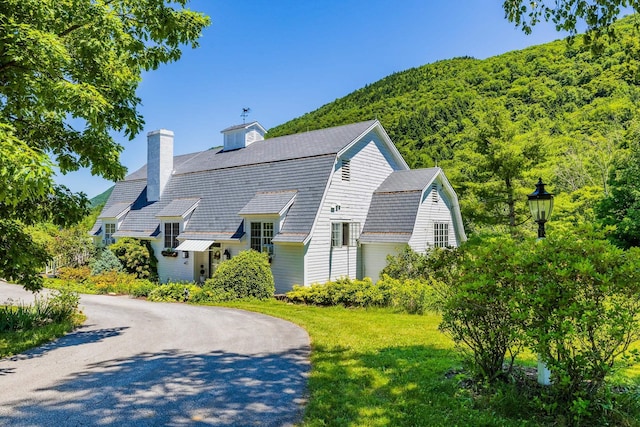 view of front of property featuring a chimney, curved driveway, a gambrel roof, and a front yard
