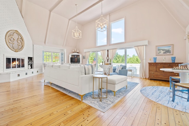 living area featuring high vaulted ceiling, hardwood / wood-style flooring, a notable chandelier, and a brick fireplace