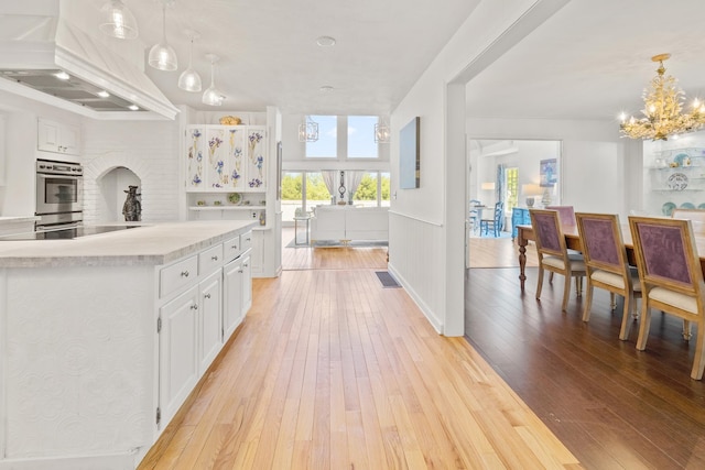 kitchen featuring oven, custom exhaust hood, light wood-style flooring, light countertops, and white cabinets