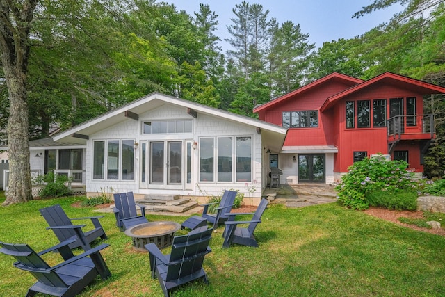 back of house featuring a lawn, a sunroom, a patio, and a fire pit