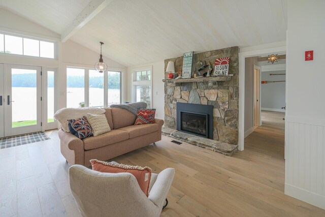 living room with french doors, lofted ceiling with beams, a stone fireplace, a water view, and light hardwood / wood-style flooring