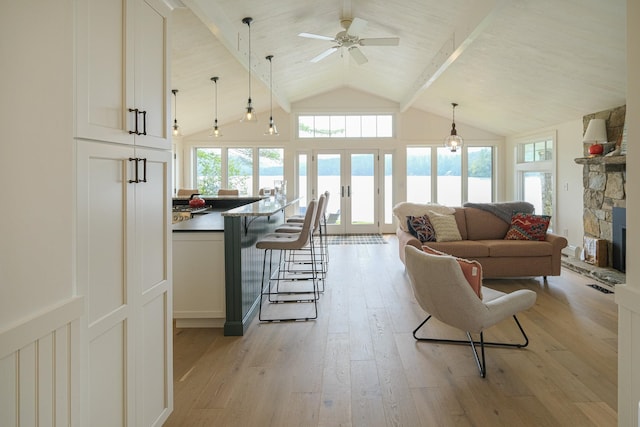 living room featuring french doors, ceiling fan, light hardwood / wood-style flooring, vaulted ceiling with beams, and a stone fireplace