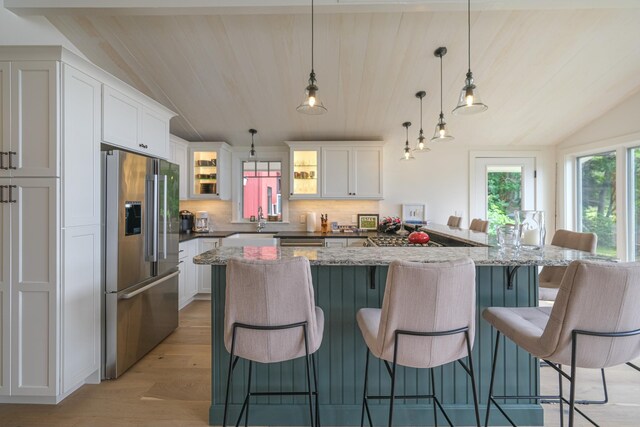 kitchen featuring high end refrigerator, a breakfast bar, vaulted ceiling, decorative light fixtures, and white cabinetry