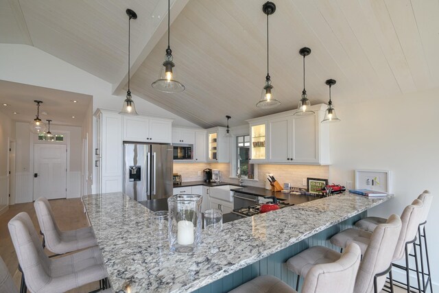 kitchen featuring kitchen peninsula, vaulted ceiling, a kitchen bar, white cabinets, and appliances with stainless steel finishes