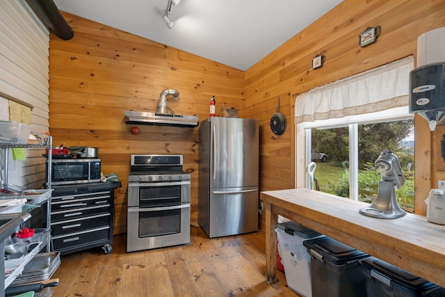 kitchen featuring light wood finished floors, wooden walls, vaulted ceiling, stainless steel appliances, and under cabinet range hood