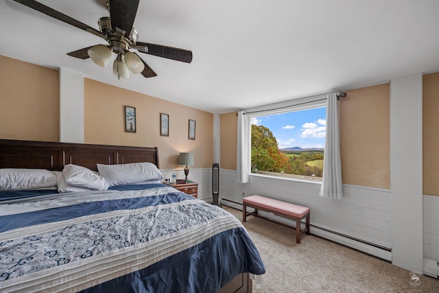 carpeted bedroom with a wainscoted wall, a baseboard radiator, a ceiling fan, and wooden walls