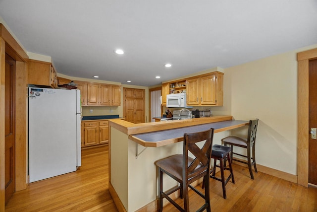 kitchen with a peninsula, white appliances, light wood-type flooring, and a kitchen breakfast bar