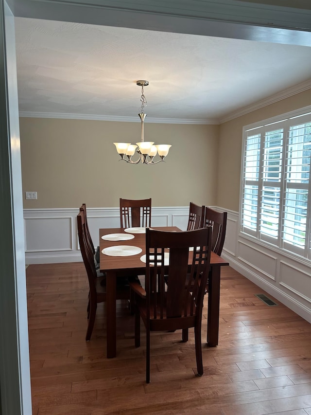 dining space with wood-type flooring, an inviting chandelier, and ornamental molding