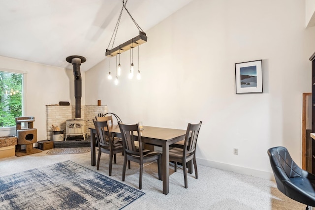 dining area featuring carpet, vaulted ceiling, and a wood stove