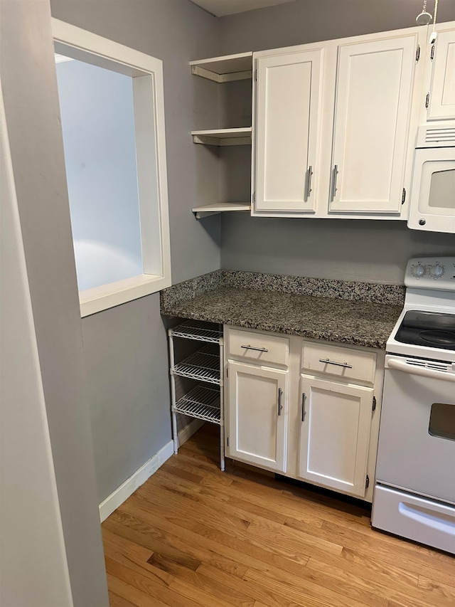 kitchen with white cabinets, dark stone counters, light hardwood / wood-style flooring, and white appliances