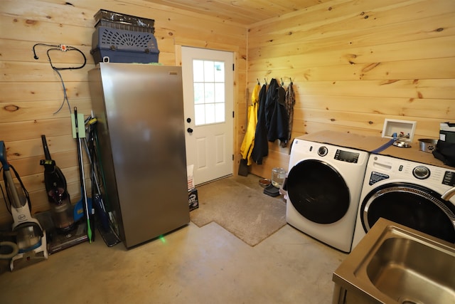 laundry room with wood walls, washing machine and dryer, and sink