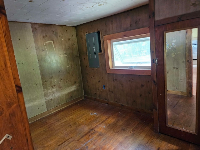 empty room with electric panel, dark hardwood / wood-style floors, and wood walls