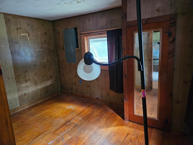 empty room featuring wood walls, light hardwood / wood-style floors, and electric panel