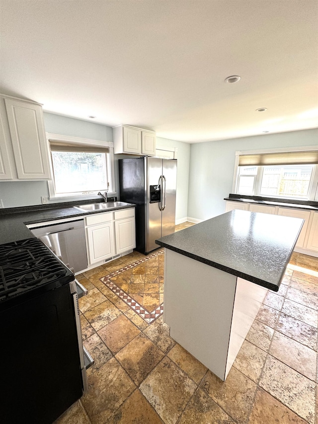 kitchen featuring appliances with stainless steel finishes, white cabinetry, sink, tile patterned floors, and a kitchen island