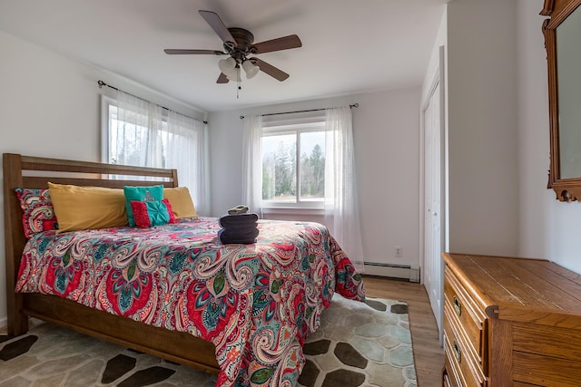 bedroom featuring ceiling fan, light hardwood / wood-style flooring, a closet, and baseboard heating