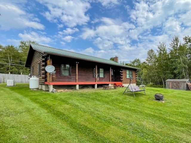 rear view of house with a fire pit, a shed, and a yard