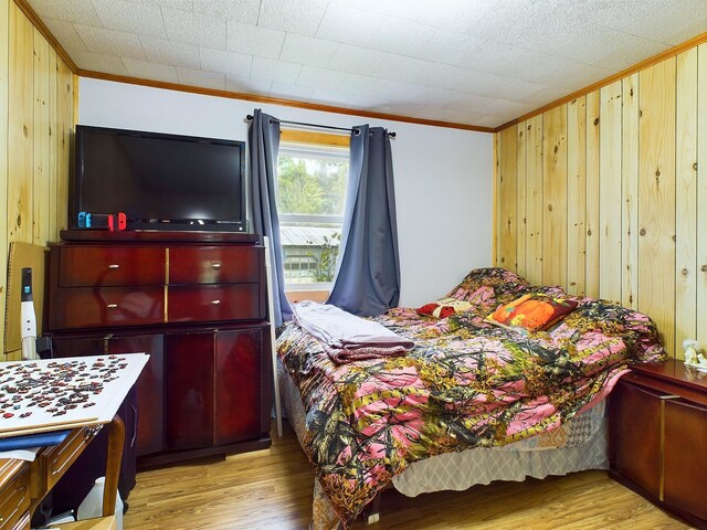 bedroom with wooden walls, light hardwood / wood-style floors, and ornamental molding