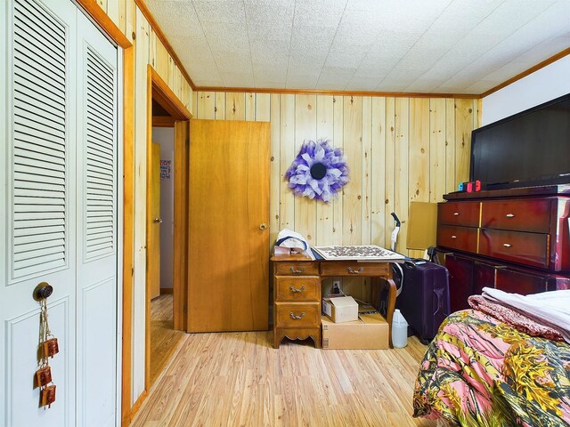 bedroom featuring a closet, light hardwood / wood-style flooring, crown molding, and wooden walls